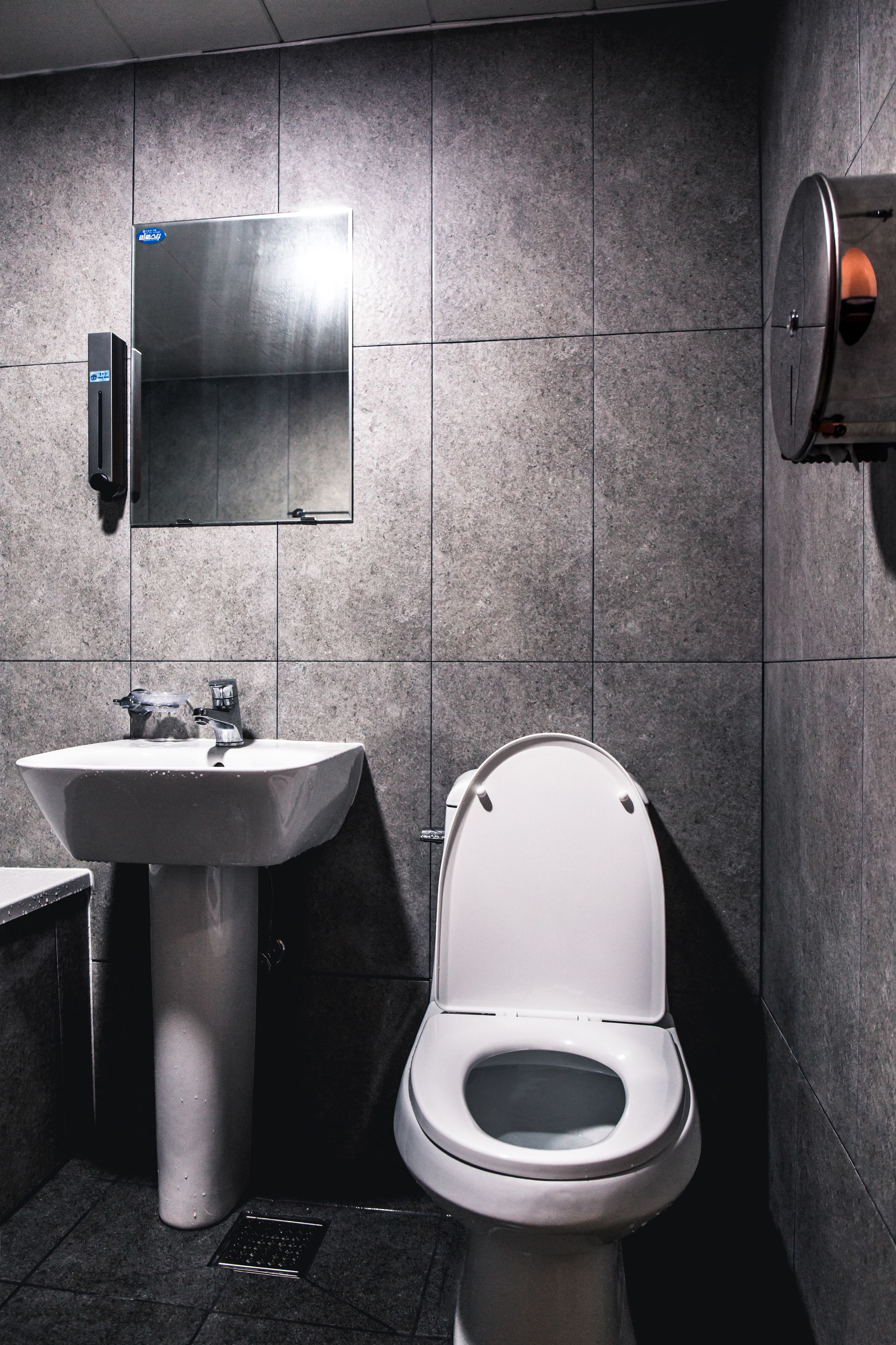 A modern bathroom with a white sink, a toilet, and a hand dryer.