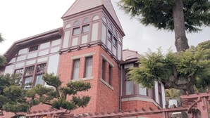 Un edificio de estilo japonés tradicional con fachada de ladrillo rojo, una torre destacada con veleta y un cartel que indica el nombre 'Athenai'.