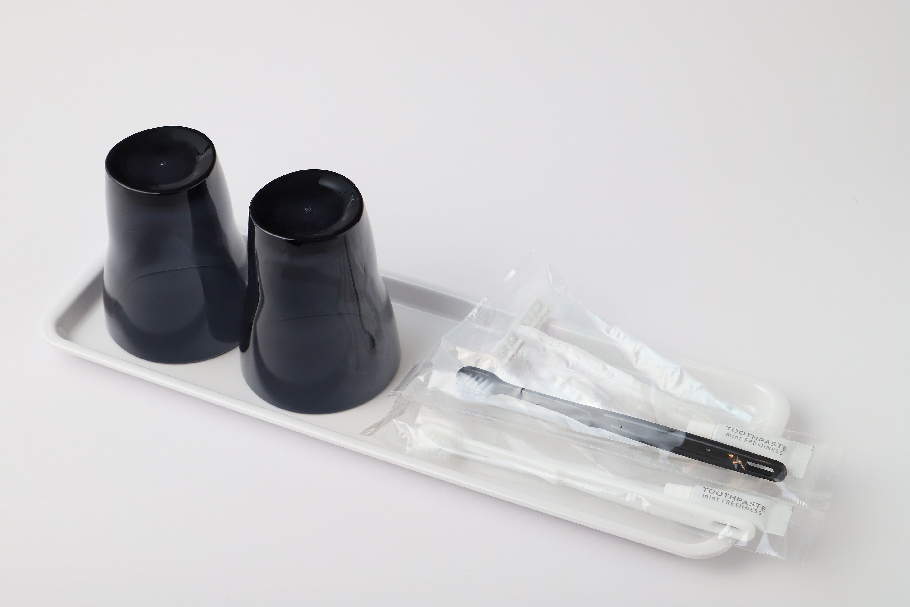 Un plateau avec deux tasses noires et une brosse à dents, le tout dans un sac en plastique transparent.