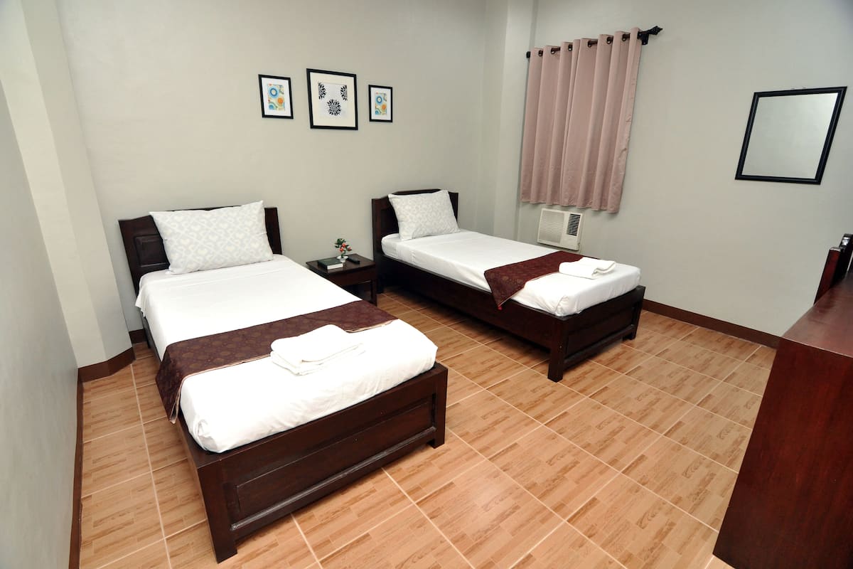 A hotel room with two beds, a bedside table, a mirror, and a window with curtains.