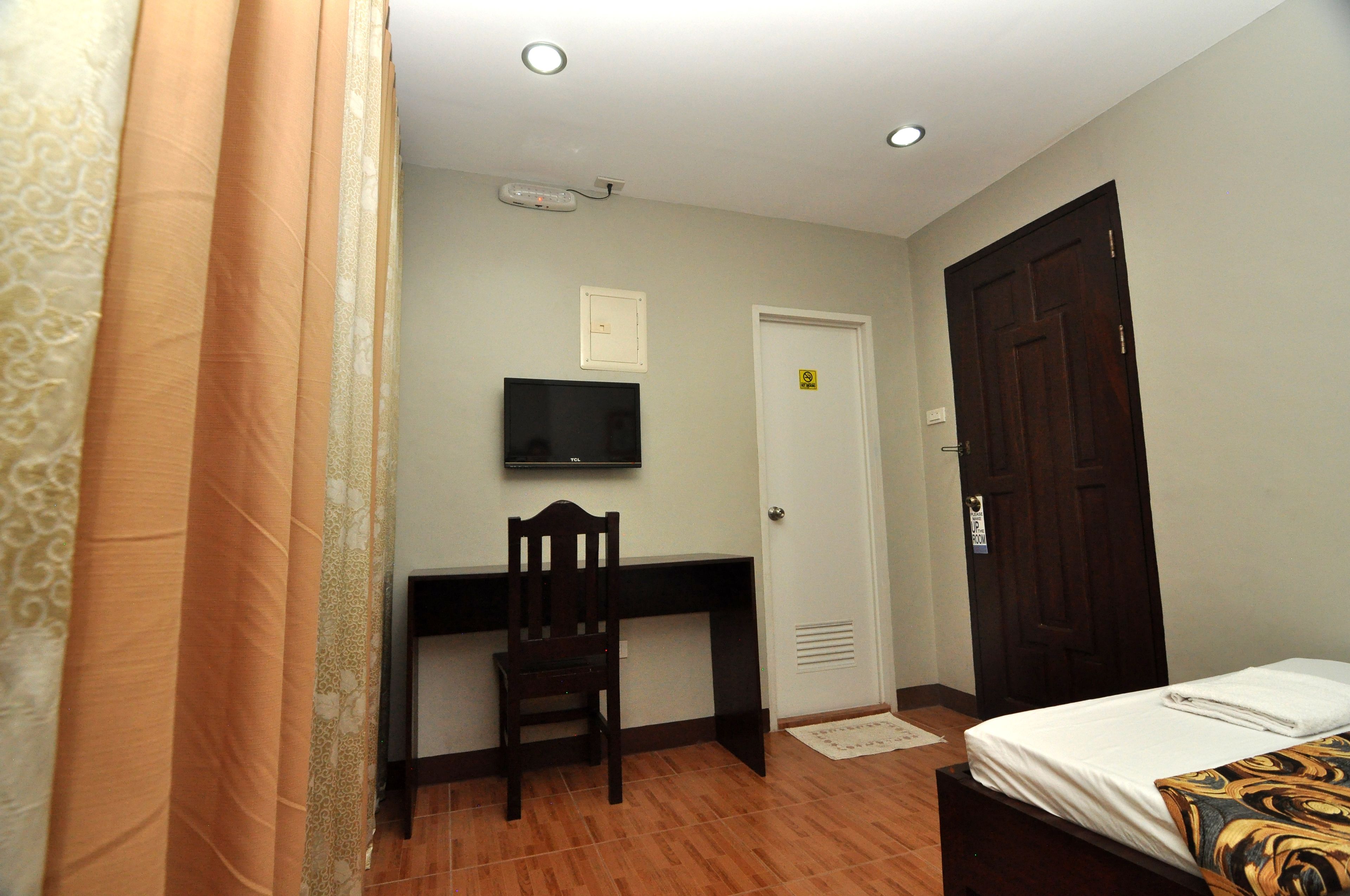 Un dormitorio con cama, escritorio, silla, televisor y puerta.