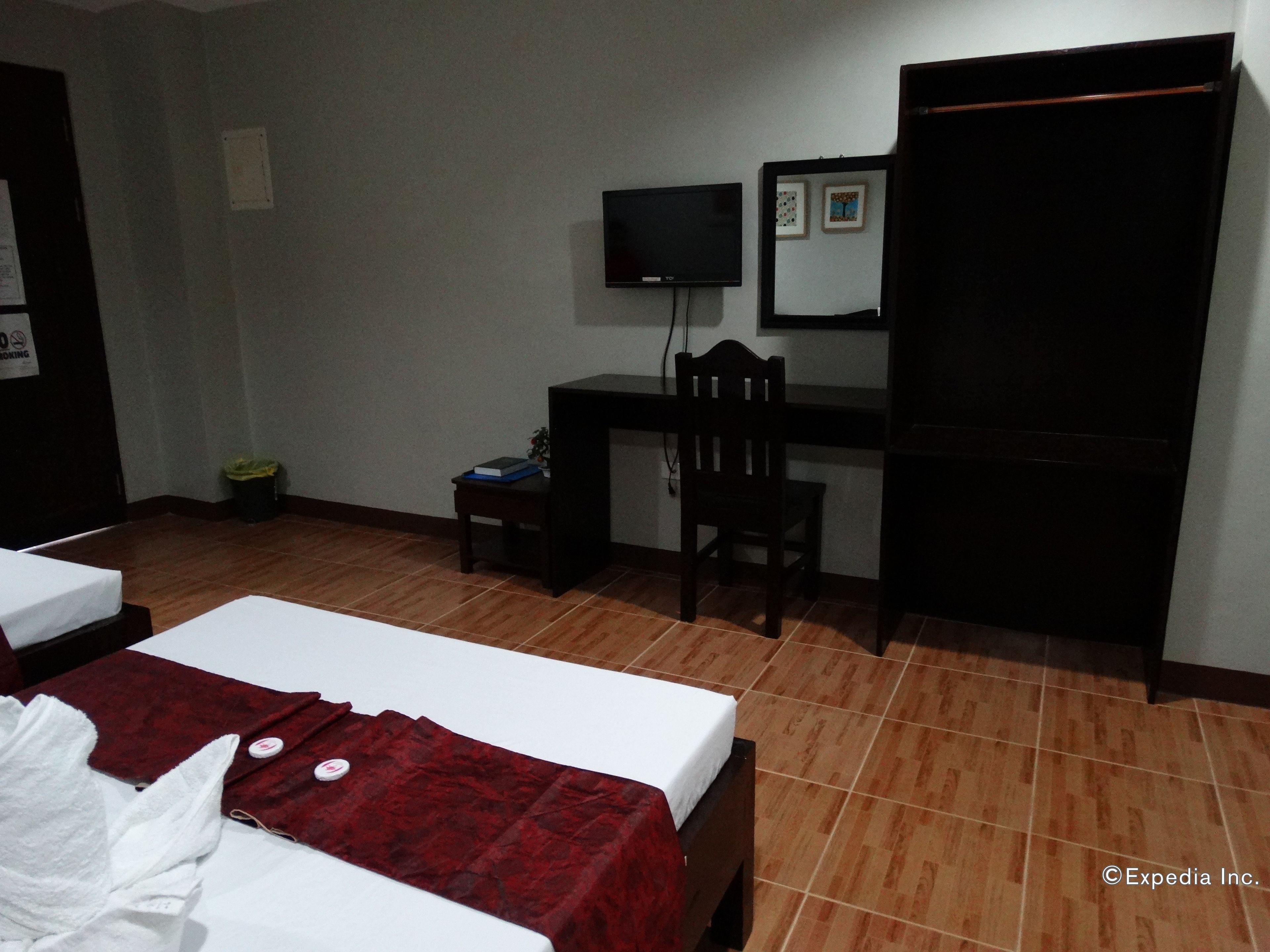 A hotel room with two beds, a desk, a chair, a TV, and a wardrobe.