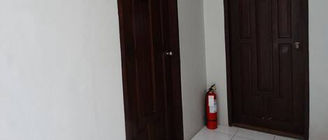 Un couloir avec deux portes en bois sombre et un extincteur rouge posé sur le sol.