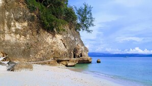 Une plage côtière avec une falaise rocheuse, une eau cristalline et un bateau visible au loin.