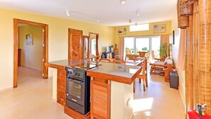 Une cuisine spacieuse dotée de meubles en bois et d’un îlot central, un coin repas avec une table et des chaises, et une grande fenêtre qui laisse entrer la lumière naturelle.