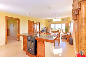Una cocina amplia con armarios de madera y una isla central, un comedor con mesa y sillas, y un ventanal que proporciona luz natural.
