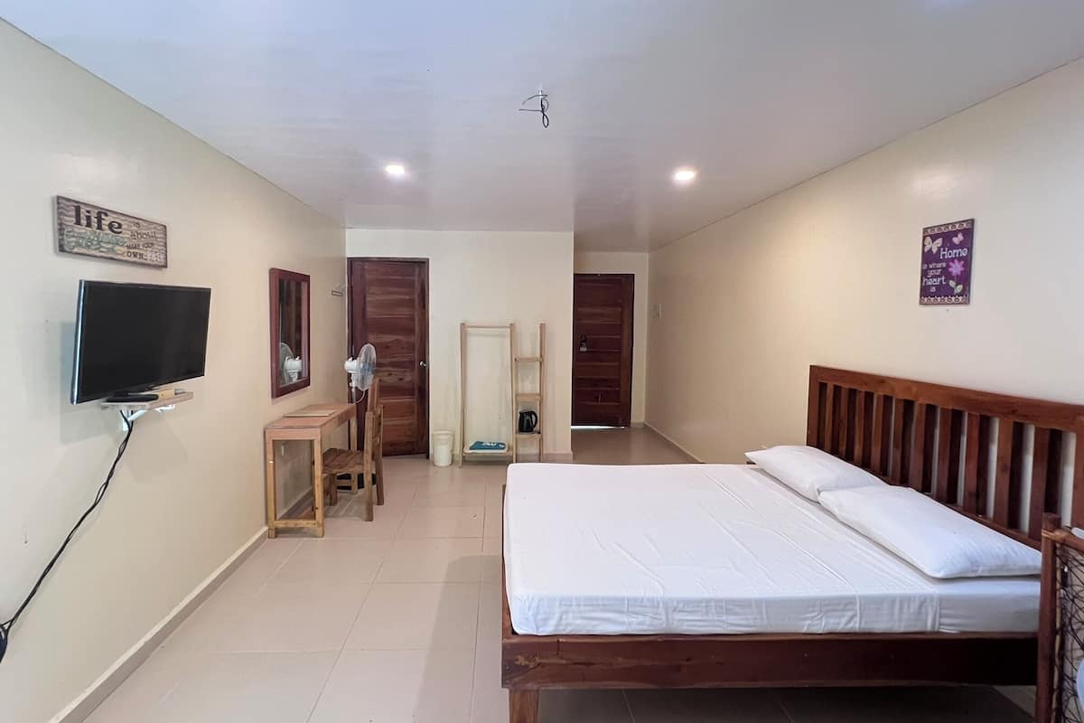 Une chambre à coucher comprenant un lit, un téléviseur fixé au mur, une chaise en bois, une petite table et une porte donnant sur une autre pièce.
