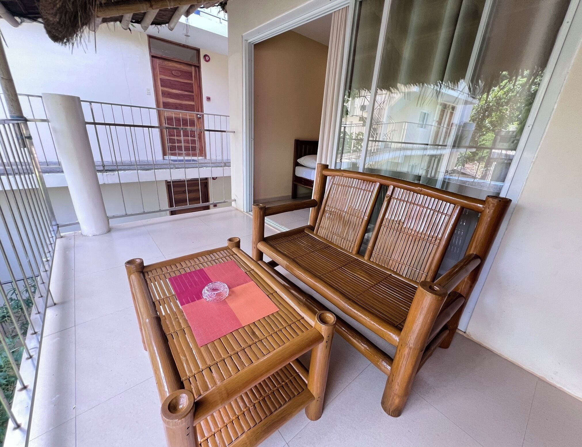 Un balcon avec un banc et une table en bois, une rambarde en métal et une vue sur un immeuble situé de l’autre côté de la rue.