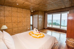 Habitación de hotel con una cama grande, vista al mar y una pared con motivos de bambú.