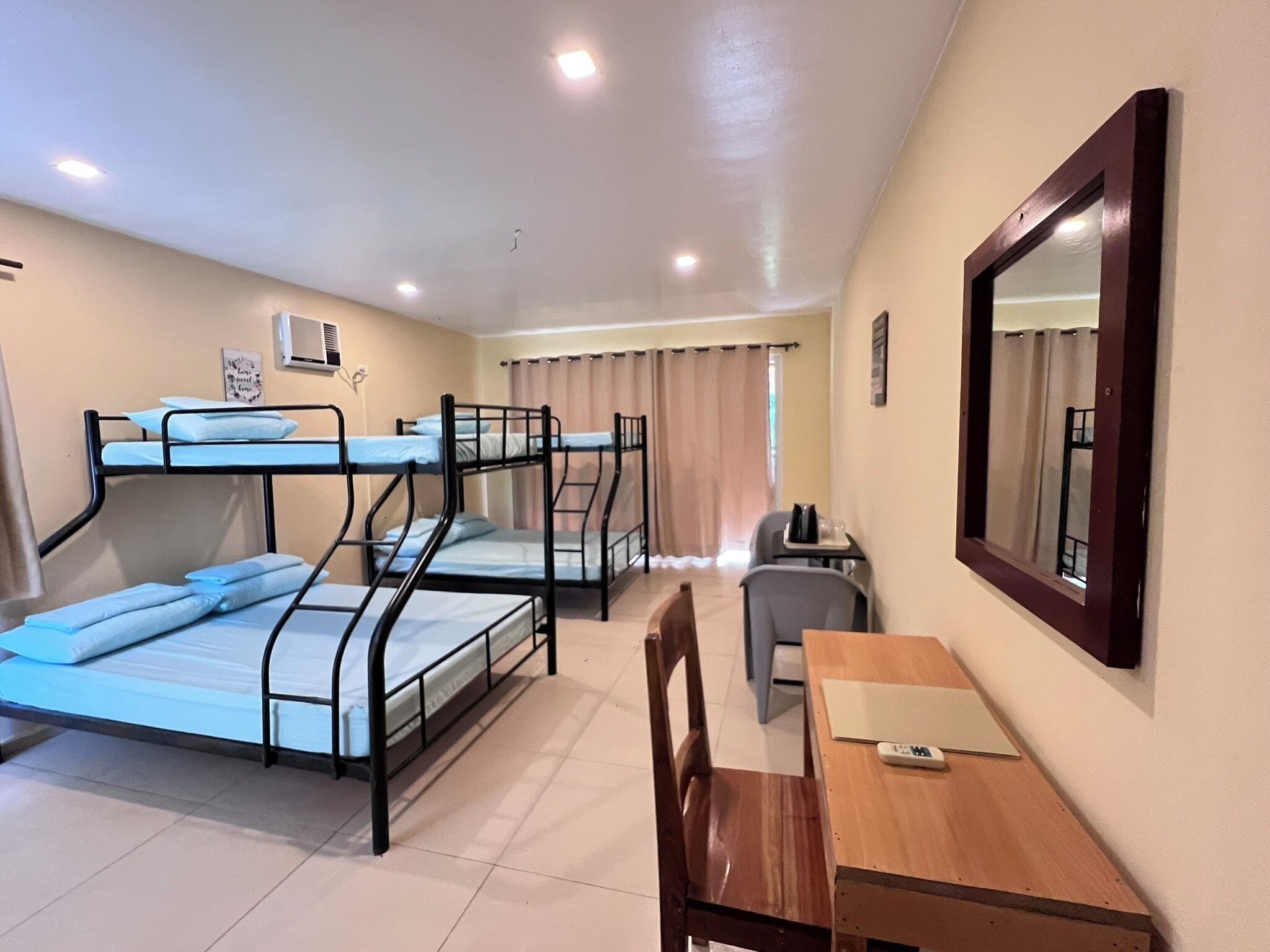 A dormitory room with bunk beds, a desk, a chair, and a mirror.