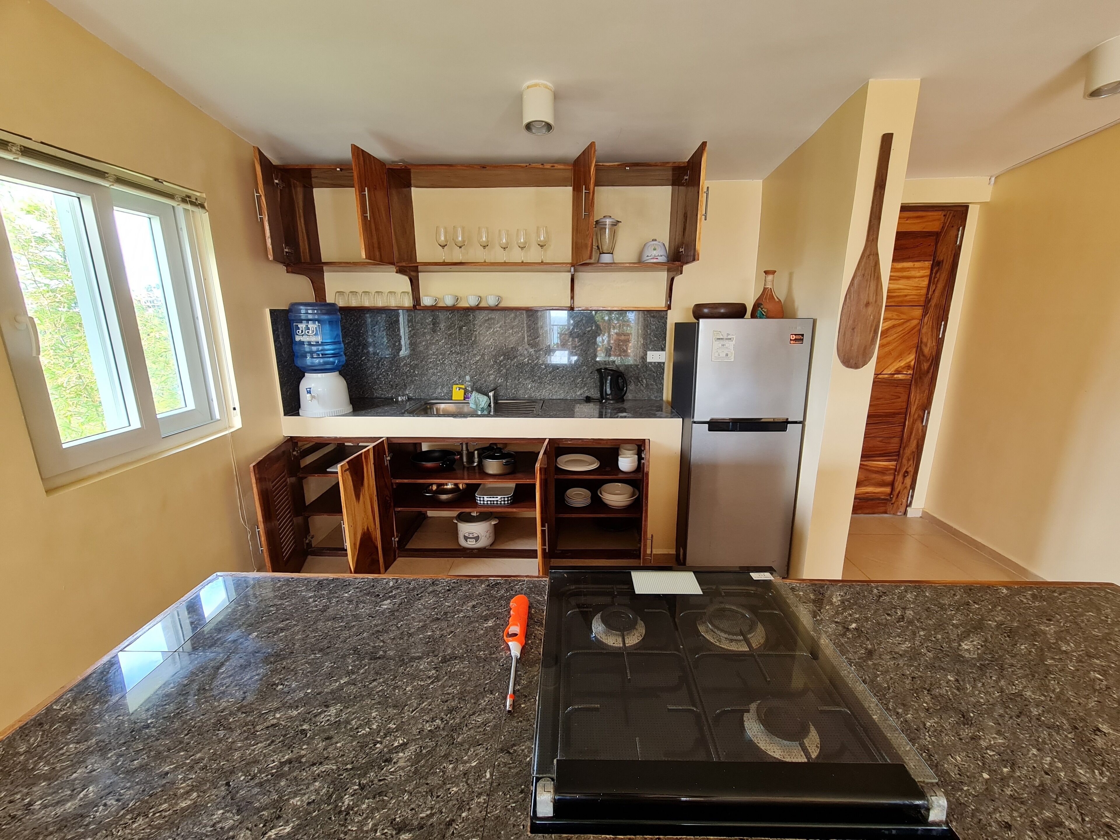 Una cocina con encimeras de granito, estufa a gas, refrigerador y armarios de madera.