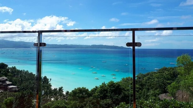 Une vue imprenable sur des eaux turquoise, parsemées de bateaux, le tout entouré d’une végétation luxuriante et sous un ciel dégagé.
