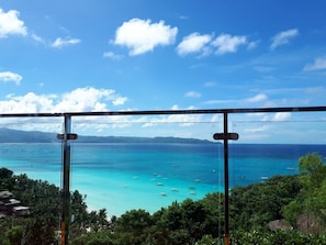 Une vue imprenable sur des eaux turquoise, parsemées de bateaux, le tout entouré d’une végétation luxuriante et sous un ciel dégagé.