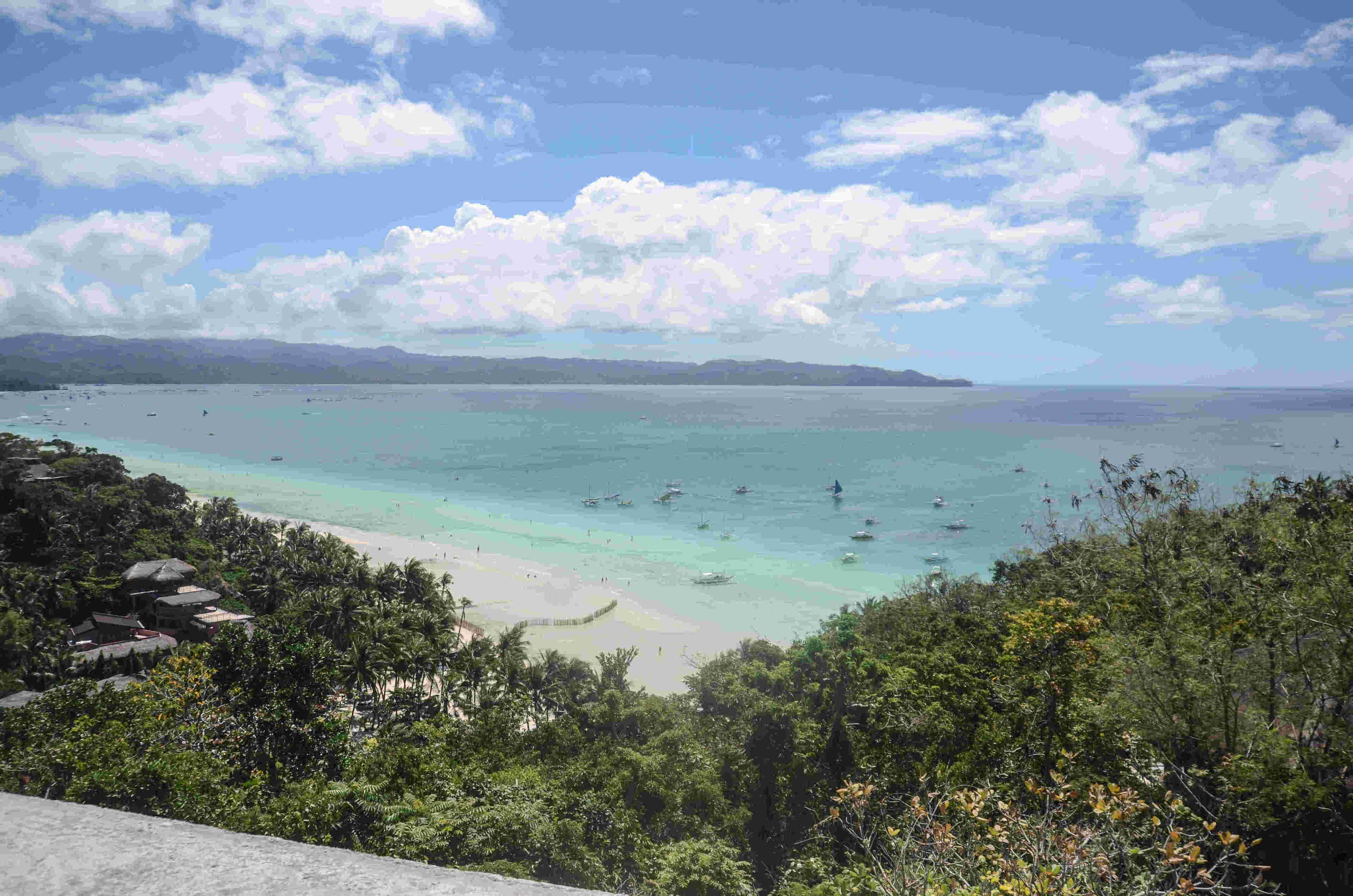 A coastal view with a beach, boats, and dense greenery.