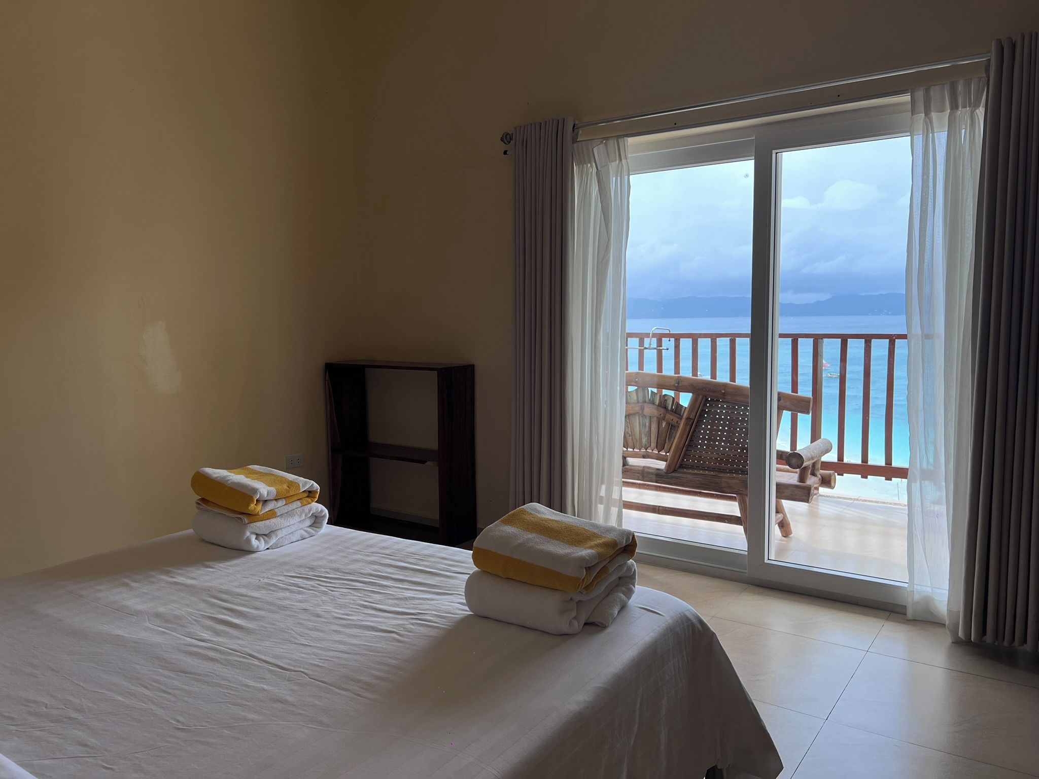 A hotel room with a bed, a small table, and a view of the sea through a sliding glass door.