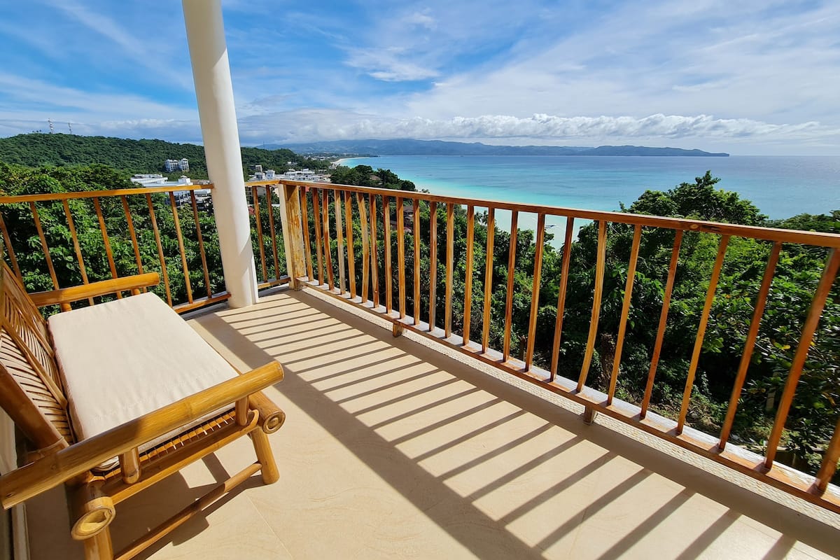 Un balcon avec une chaise en bois et une vue sur un paysage côtier.