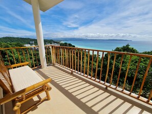 Un balcon avec une chaise en bois et une vue sur un paysage côtier.