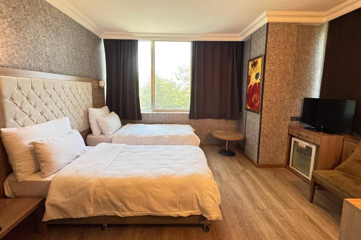 A hotel room with two beds, a television, a small table, and a window with curtains.