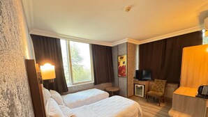 Habitación de hotel con dos camas, televisión, una mesita, una silla y escritorio con lámpara.