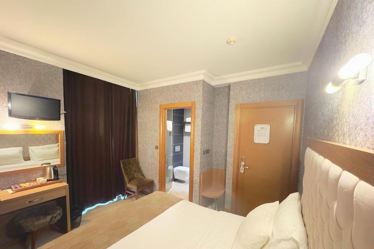 A hotel room with a bed, a desk with a chair, a television, and a door leading to another room.