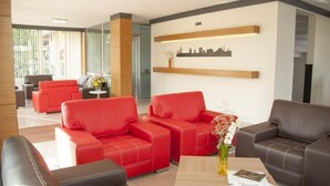 Un moderno vestíbulo de hotel con sofás de cuero rojo y marrón, una mesa de centro de madera y una obra de arte con una vista urbana en la pared.