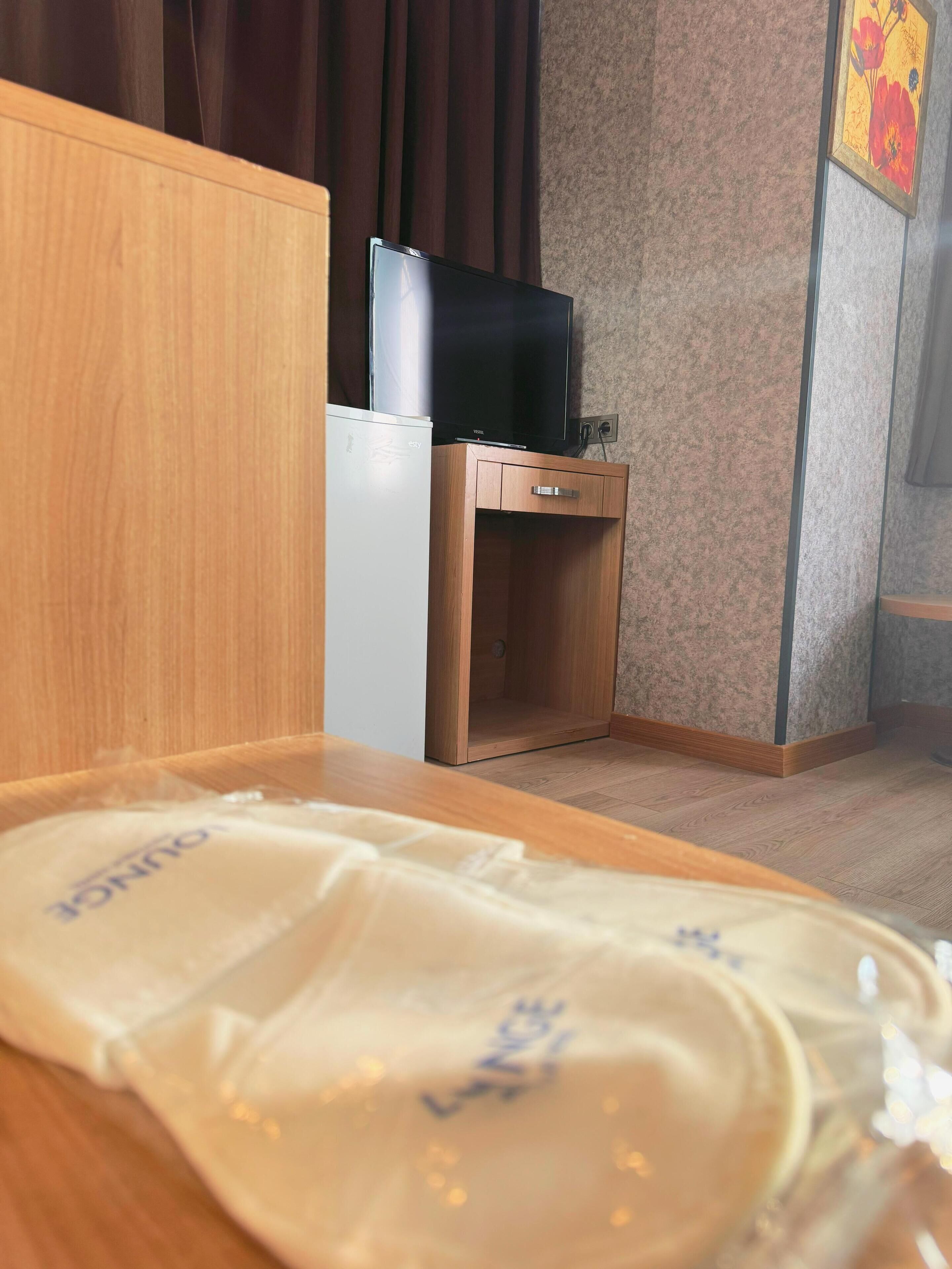 A hotel room with a bed, a small wooden cabinet, a television, and a decorative wall piece.