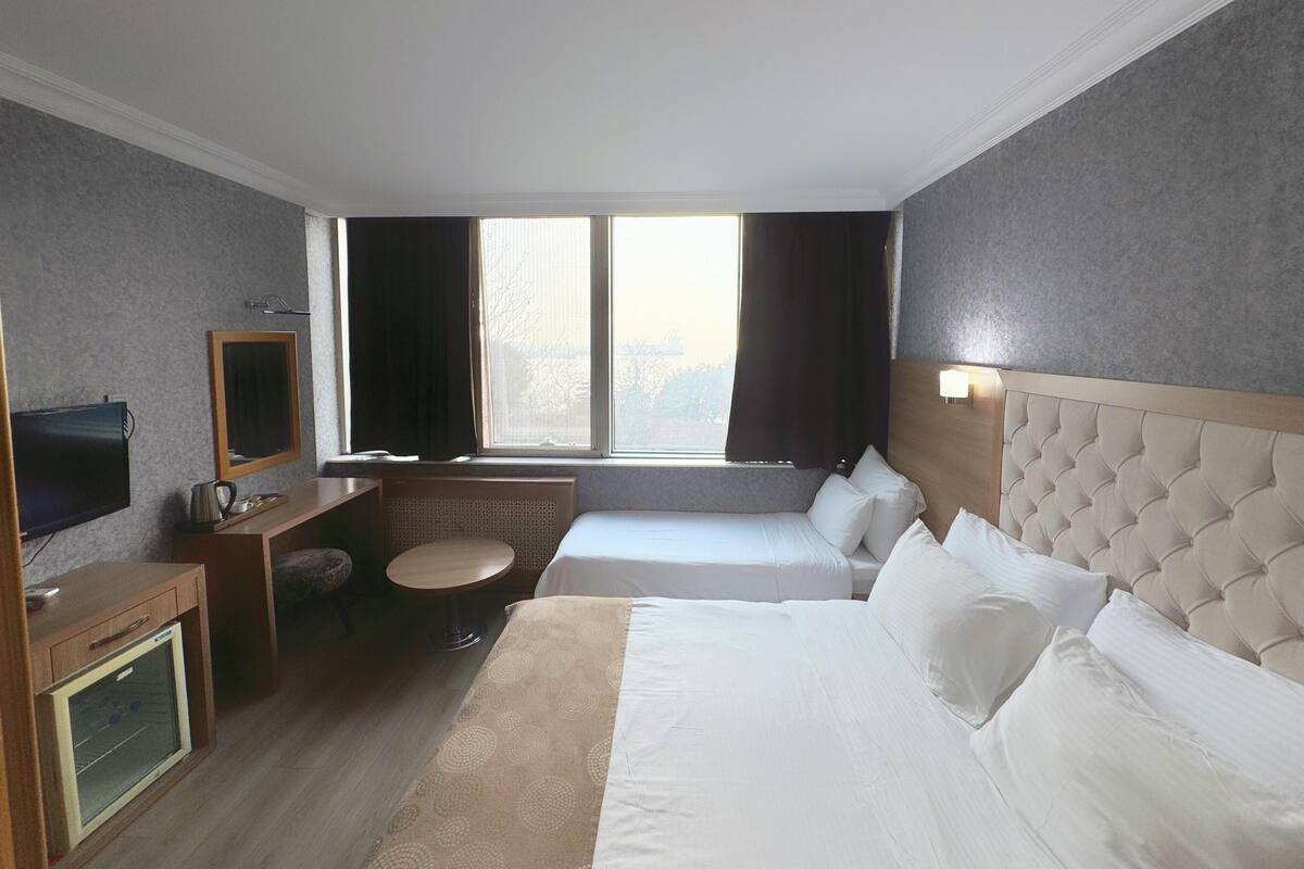 A hotel room with two beds, a TV, a small table, and a window with curtains.