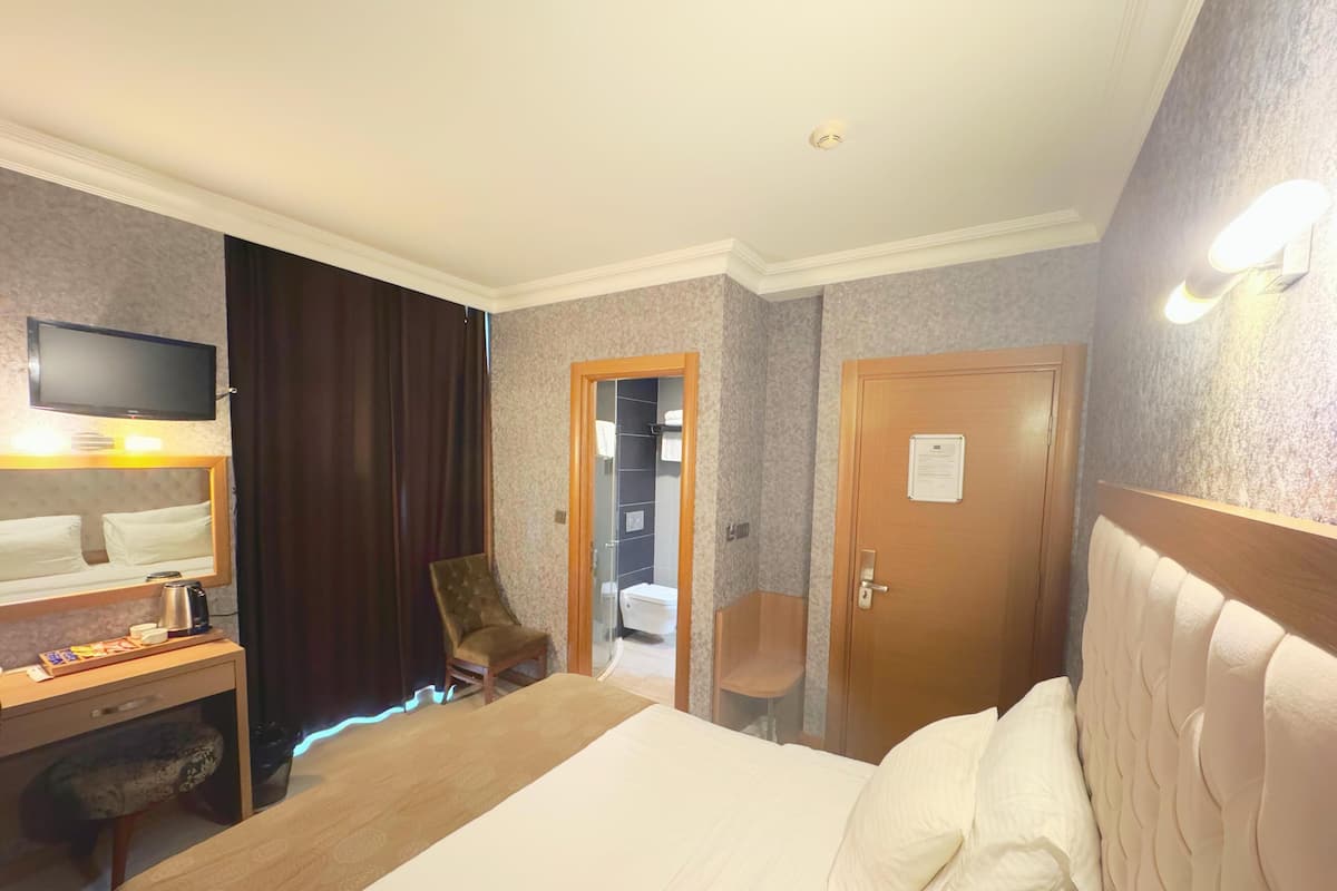 A hotel room with a bed, a desk with a chair, a television, and a door leading to a bathroom.
