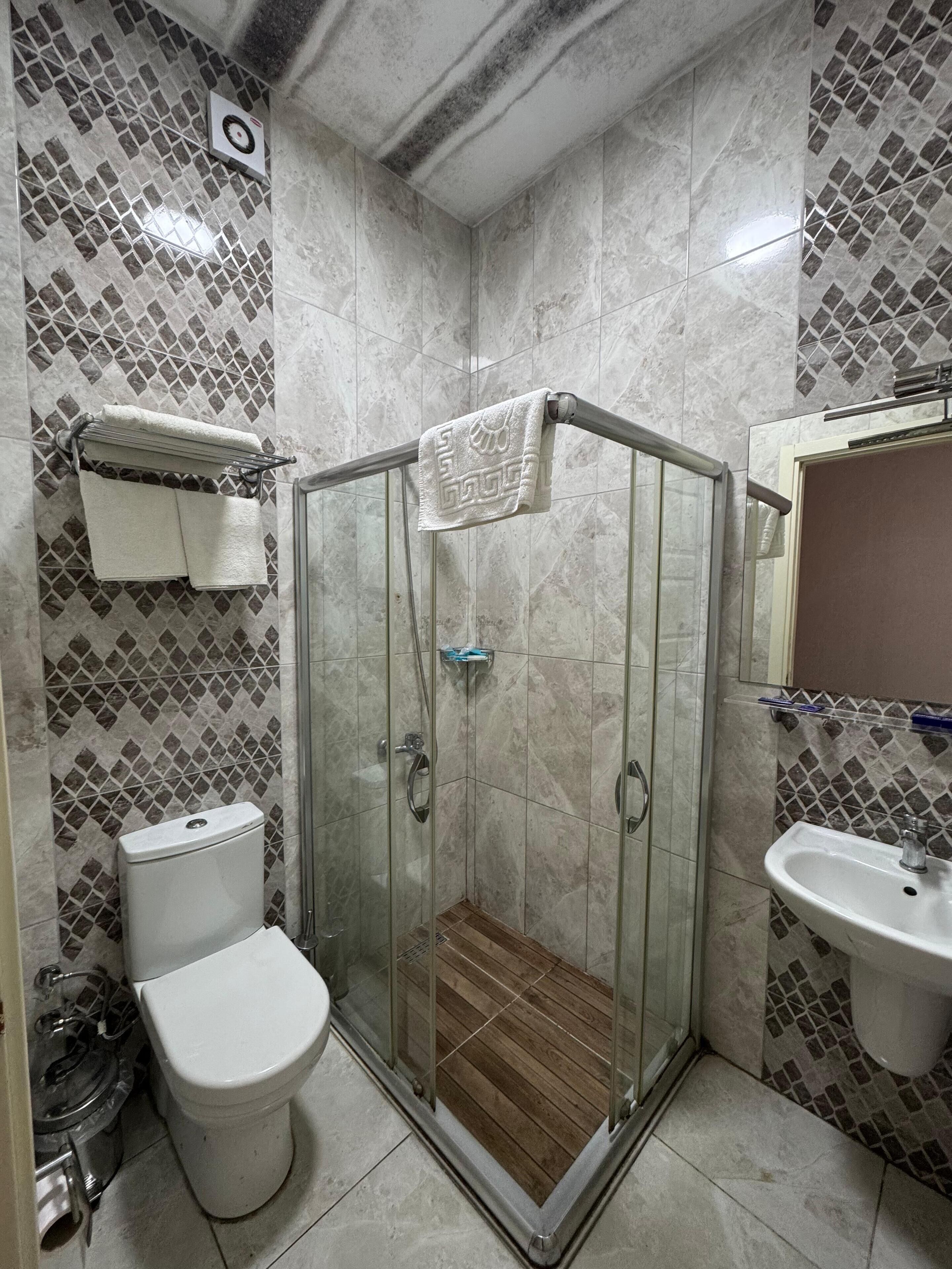 Een badkamer met een douche met glazen wand, een toilet, een wastafel en een betegelde muur met een ruitmotief.