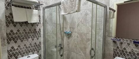Een badkamer met een douche met glazen wand, een toilet, een wastafel en een betegelde muur met een ruitmotief.