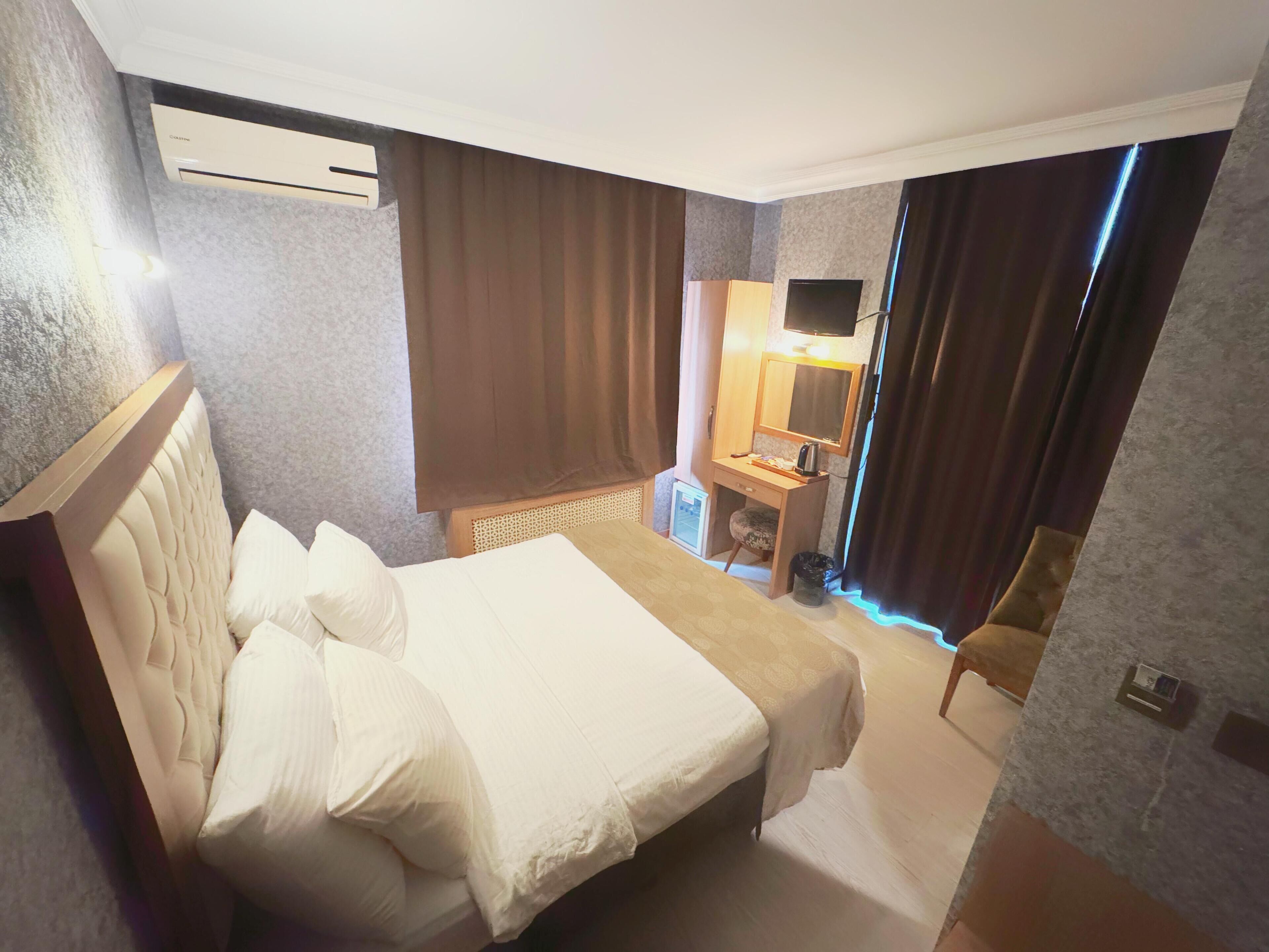 A hotel room with a bed, a desk with a chair, a television, and an air conditioning unit.