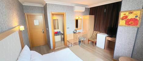 A hotel room with a bed, a desk, a chair, a TV, and a small table.
