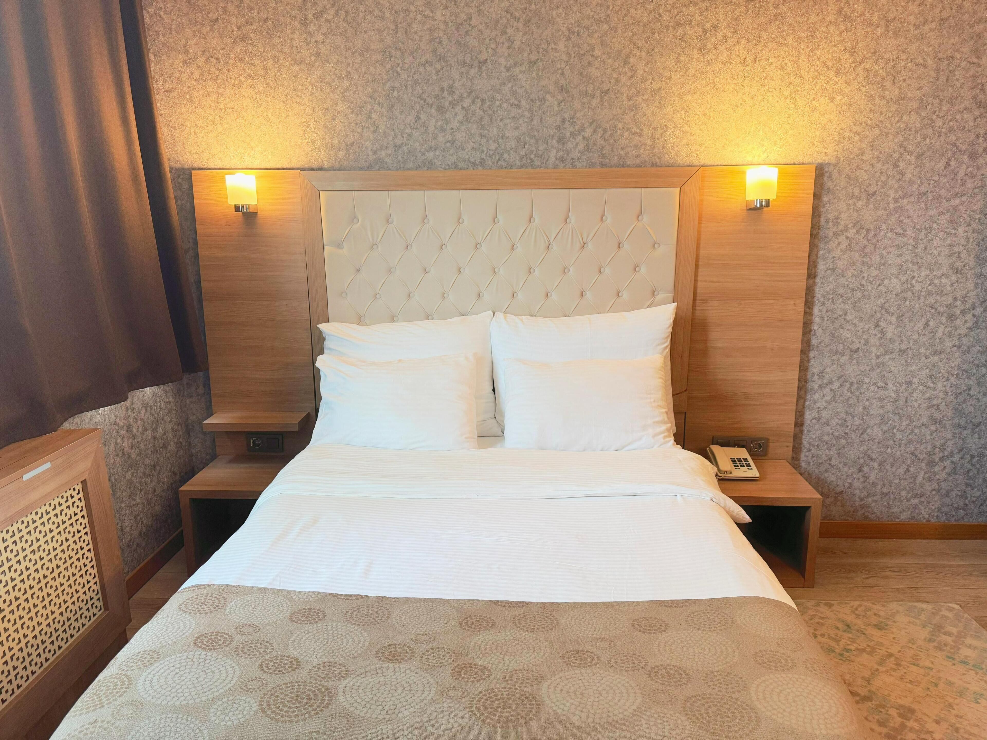 A hotel room with a tufted headboard, two bedside lamps, a bed with white linens, and a patterned throw.