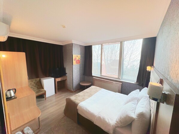 A hotel room with a bed, a desk, a chair, a small table, a radiator, and a window with a view of trees. - Lounge Boutique Hotel (Istanbul)