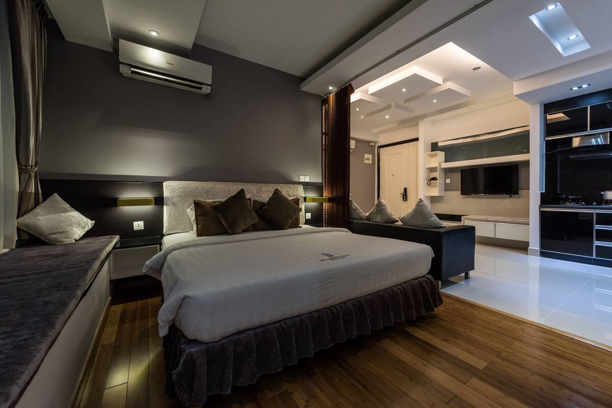 Ein modernes Schlafzimmer mit einem großen Bett, Nachttischen, einem Fernseher und einer integrierten Küchenzeile.