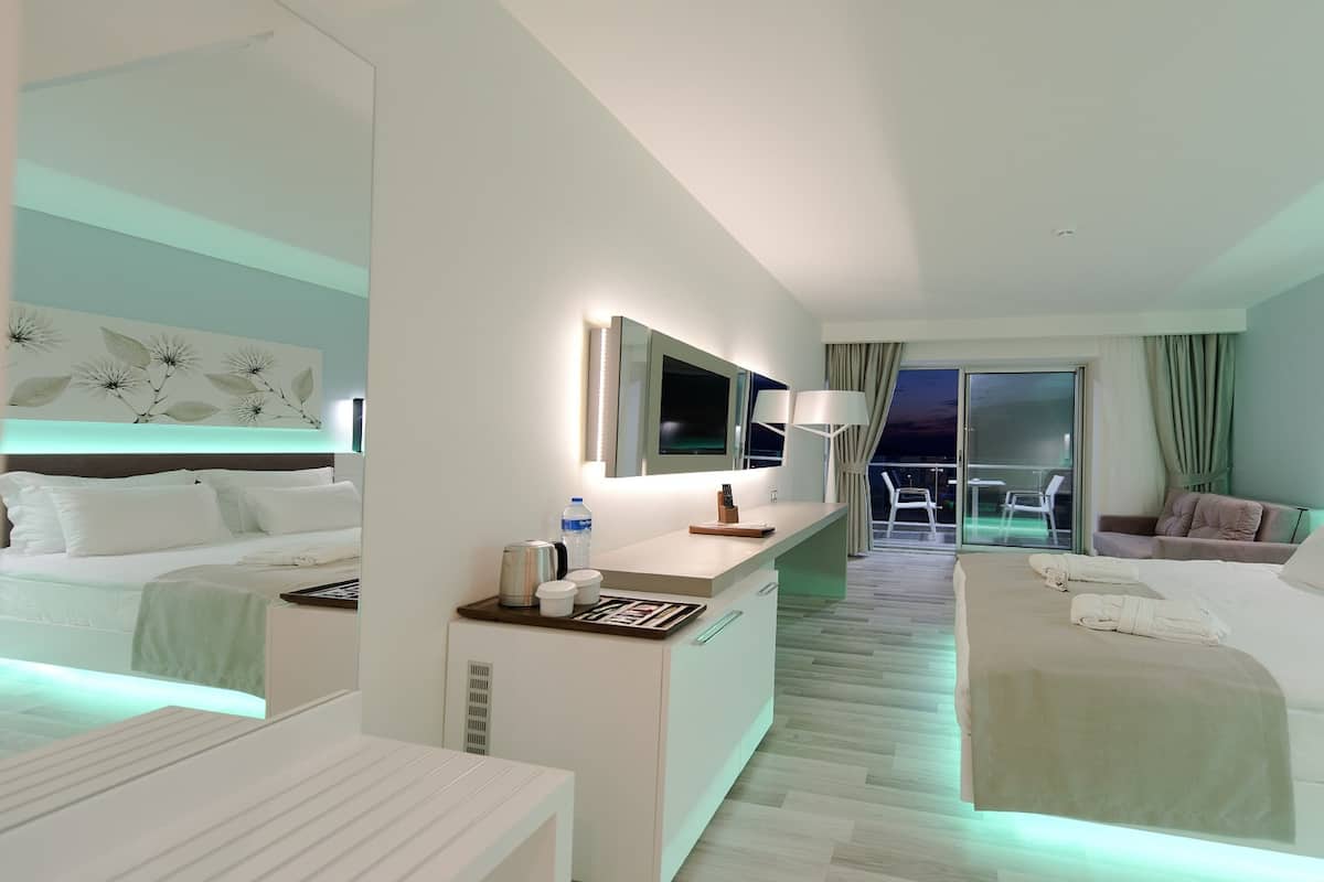 A modern hotel room with two beds, a desk with a lamp, a TV, and a balcony with a chair.