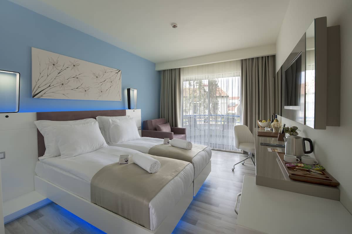 A hotel room with a bed, a desk, a chair, a TV, and a window with curtains.