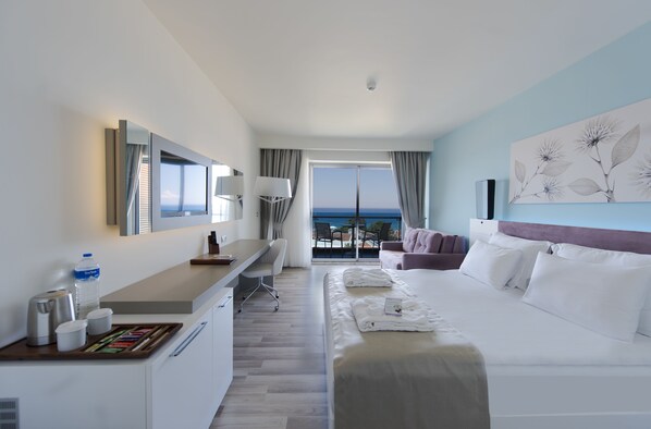 A hotel room with a bed, a desk, a chair, a TV, and a view of the ocean.