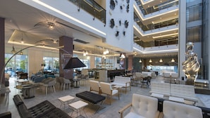 A spacious lobby with modern furniture, a bar area, and a high ceiling with decorative lighting. - Flora Garden Ephesus Hotel Kusadasiot (Kusadasi)
