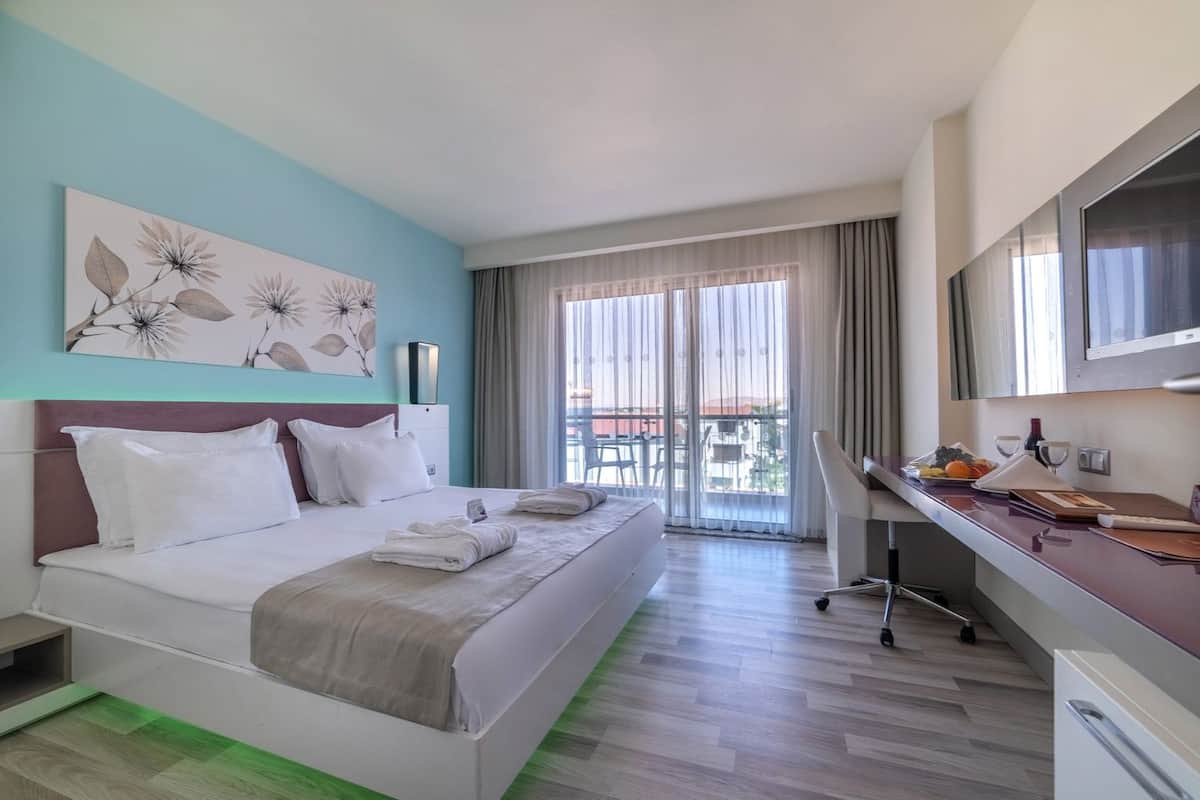 A hotel room with a bed, a desk, a chair, a TV, and a balcony with a view.