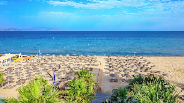 A beach with numerous umbrellas and sun loungers, a clear sky, and the sea in the background. - Flora Garden Ephesus Hotel Kusadasiot (Kusadasi)