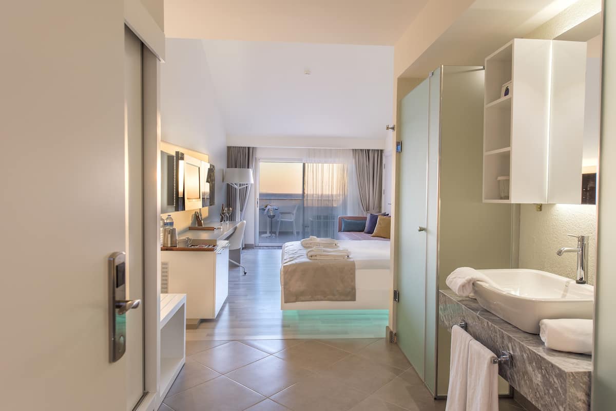 A hotel room with a bed, a desk, a bathroom with a sink, and a view of the outdoors.