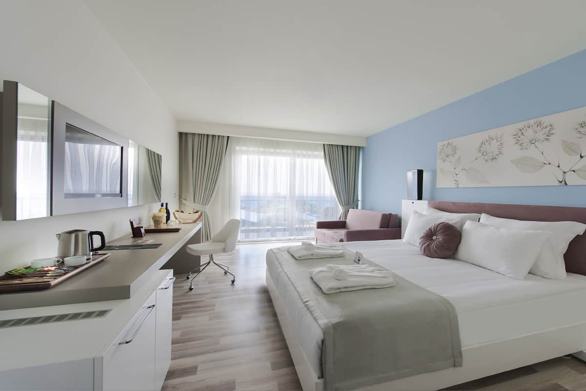 A modern hotel room with a bed, a desk, a chair, and a large window with curtains.