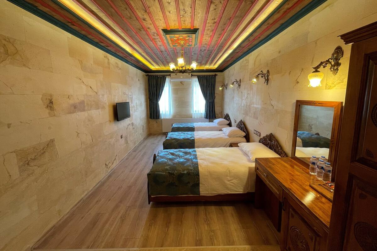 Une chambre d’hôtel avec trois lits, un plancher en bois, un lustre et un grand miroir.