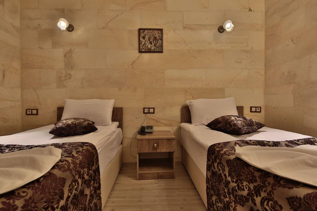 Une chambre d’hôtel avec deux lits, chacun agrémenté de draps et d’oreillers à motifs, une petite table de chevet en bois avec un téléphone et un tableau accroché au mur.
