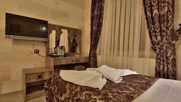 A hotel room with a bed, a TV mounted on the wall, a wooden nightstand, and a mirror.