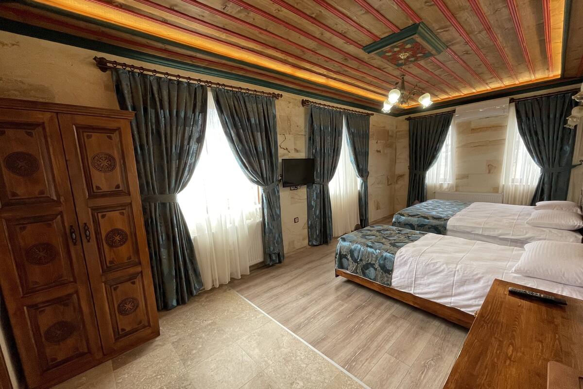 Une chambre d’hôtel avec deux lits, une armoire en bois et un téléviseur fixé au mur.
