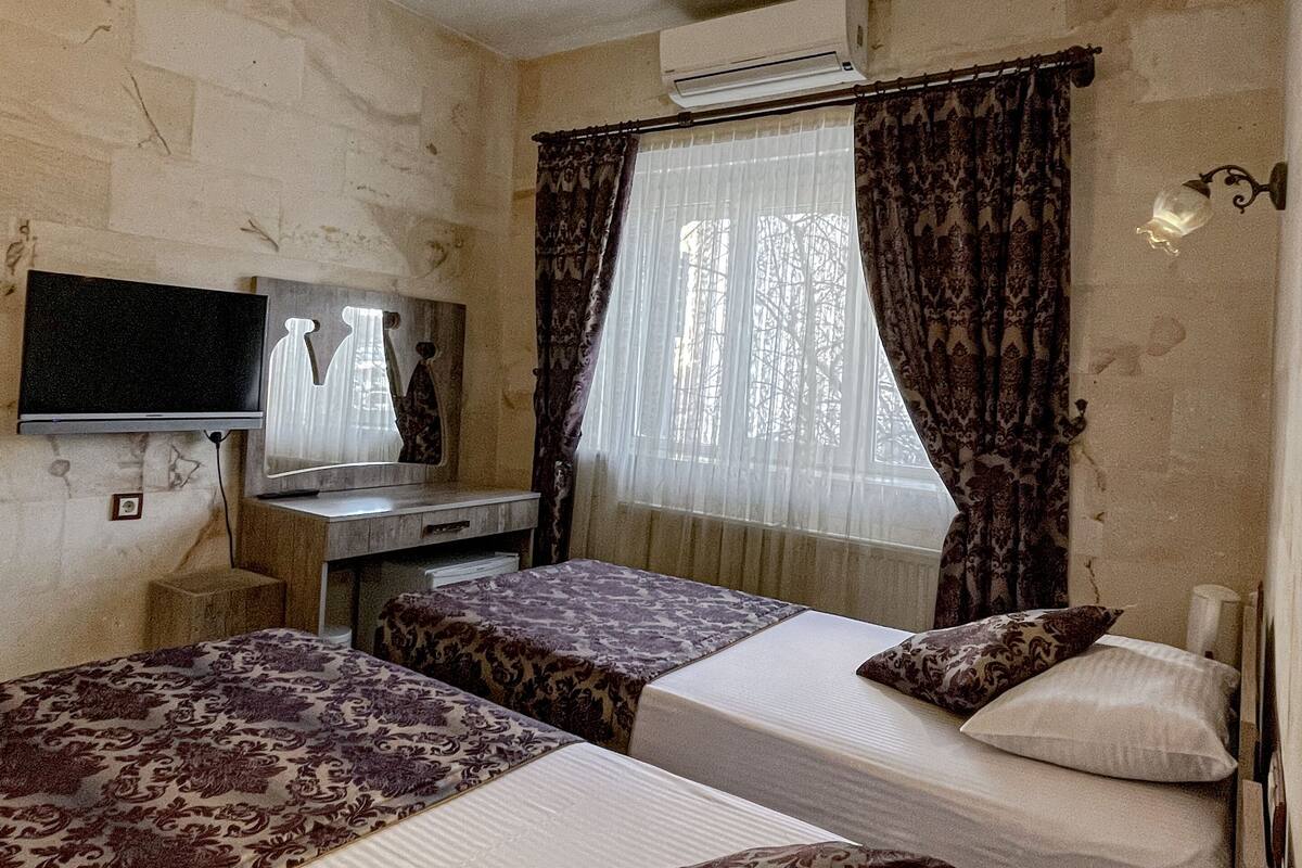 Une chambre d’hôtel avec deux lits, une télévision, un appareil de climatisation et une fenêtre avec des rideaux.