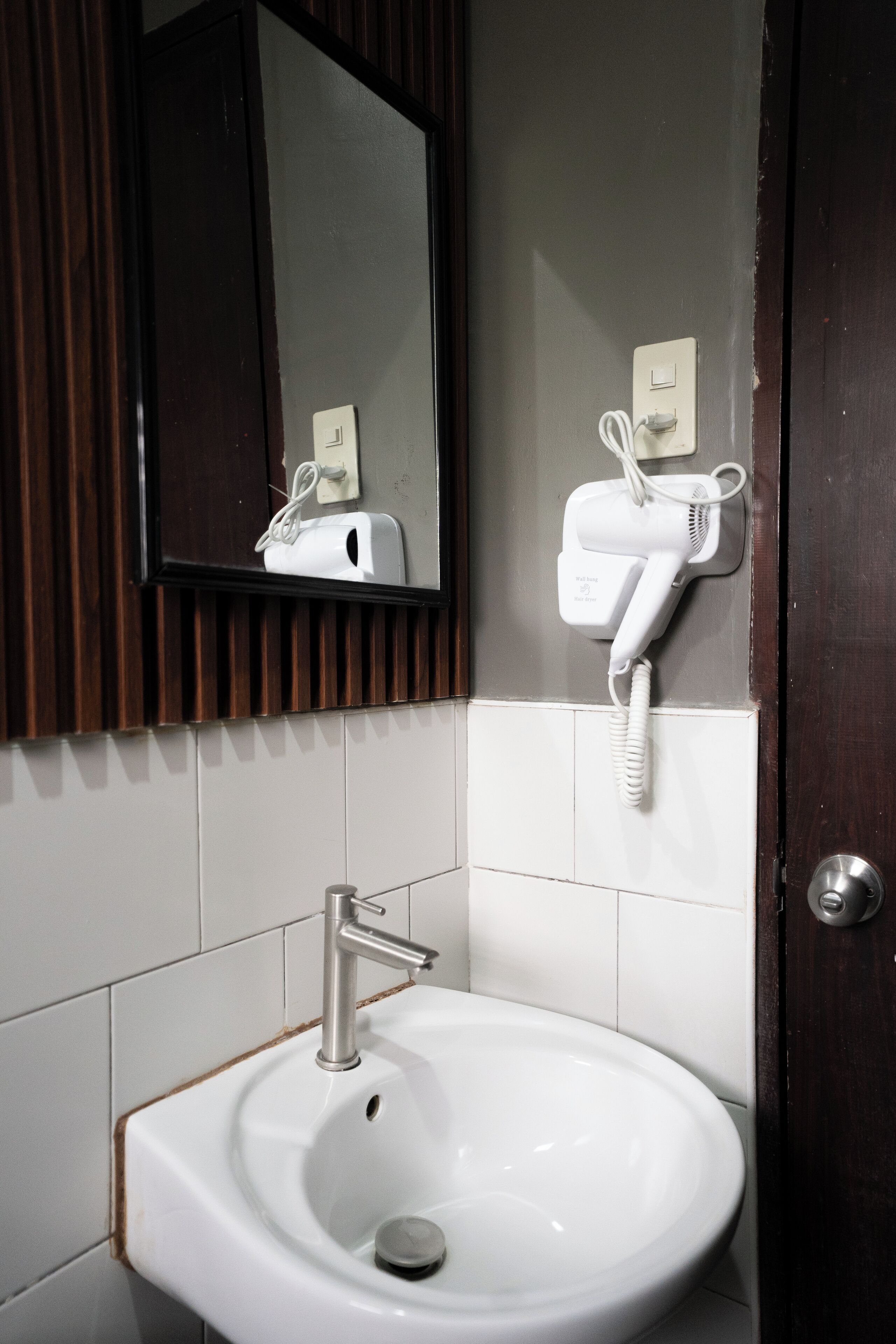 Un baño con un lavabo blanco, un espejo y un secador de pelo montado en la pared.
