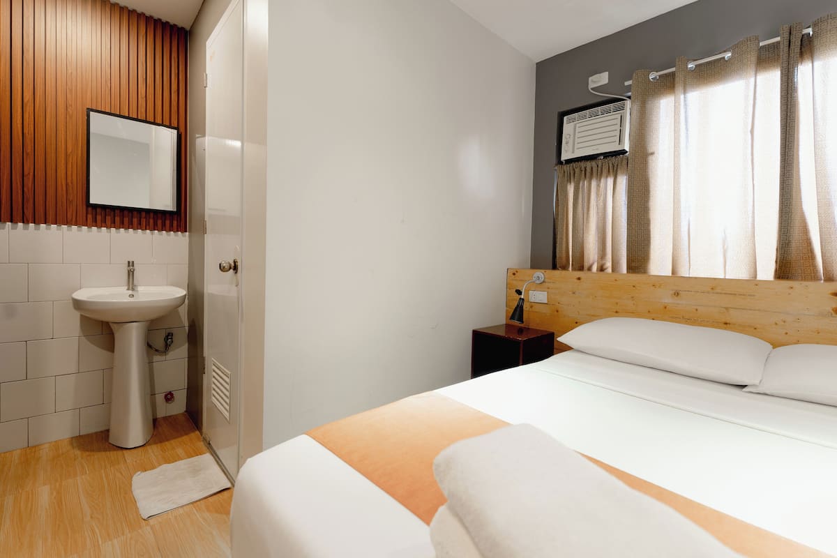 A hotel room with a wooden headboard, a white bed, a small bedside table, a white sink, and a mirror on the wall.